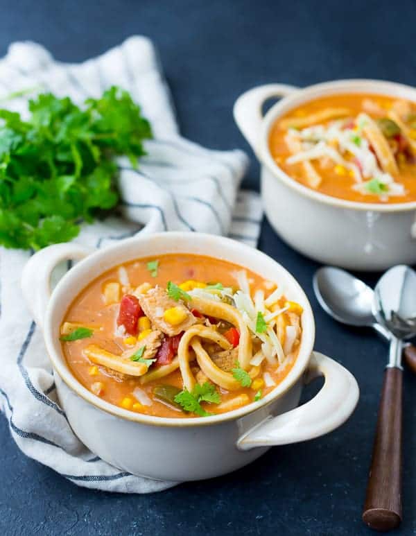 Overhead view of white soup bowl containing chicken enchilada soup. In the background is another bowl of soup, a striped cloth, and fresh cilantro.