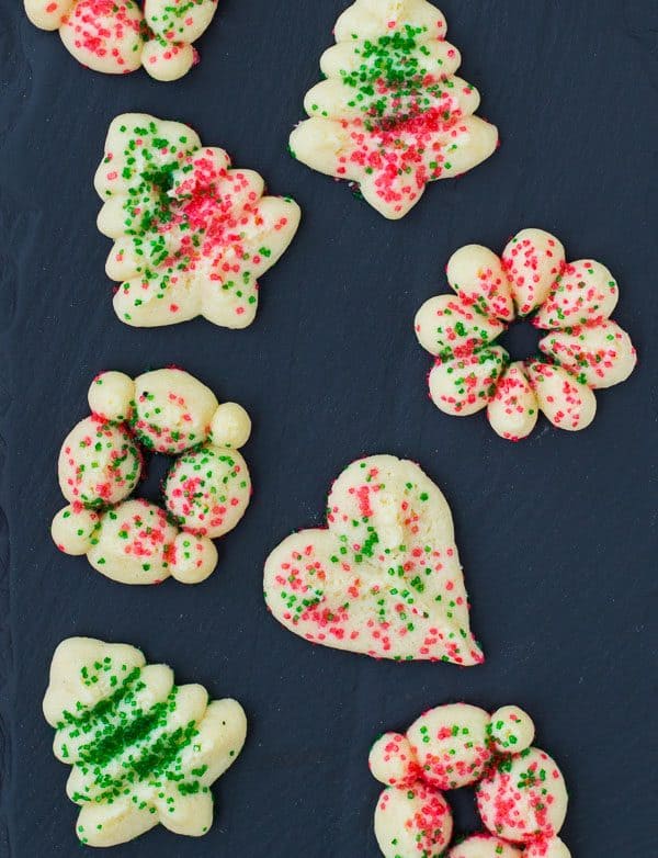 Overhead of several spritz cookies in a variety of shapes on a slate background.