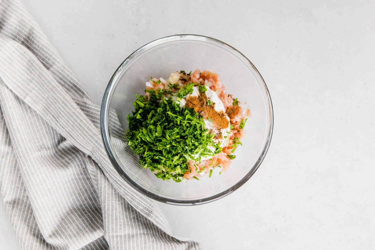 Overhead of clear glass mixing bowl containing Chicken Kofta Ingredients.