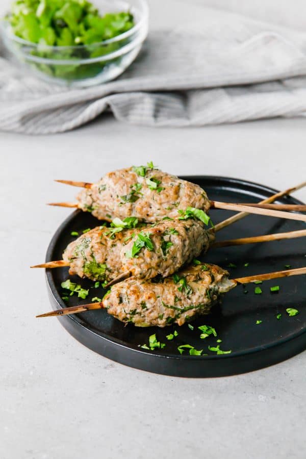 Several kofta on small black plate, garnished with chopped parsley.