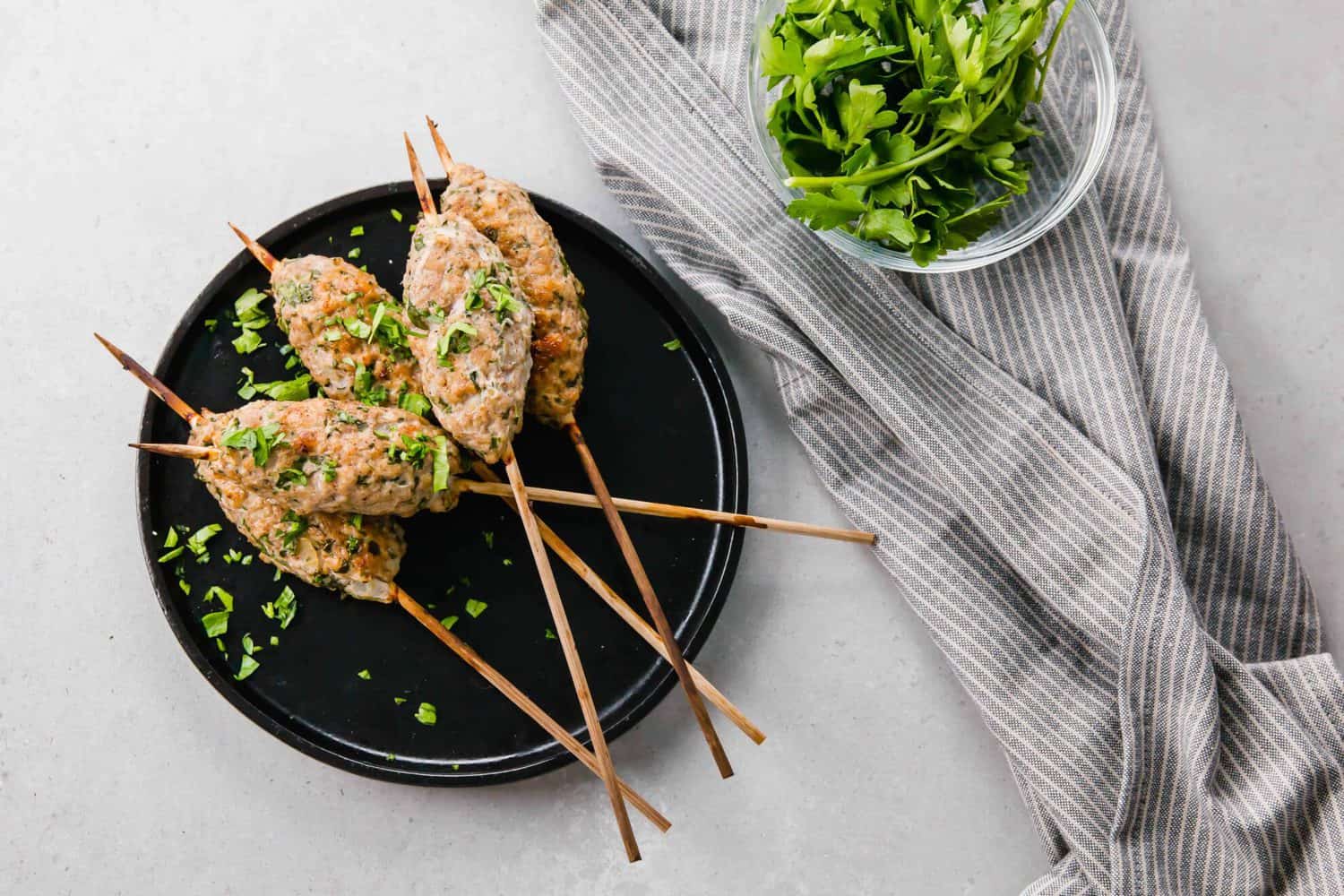 Overhead of kofta on plate with gray striped cloth nearby, along with bowl of parsley.