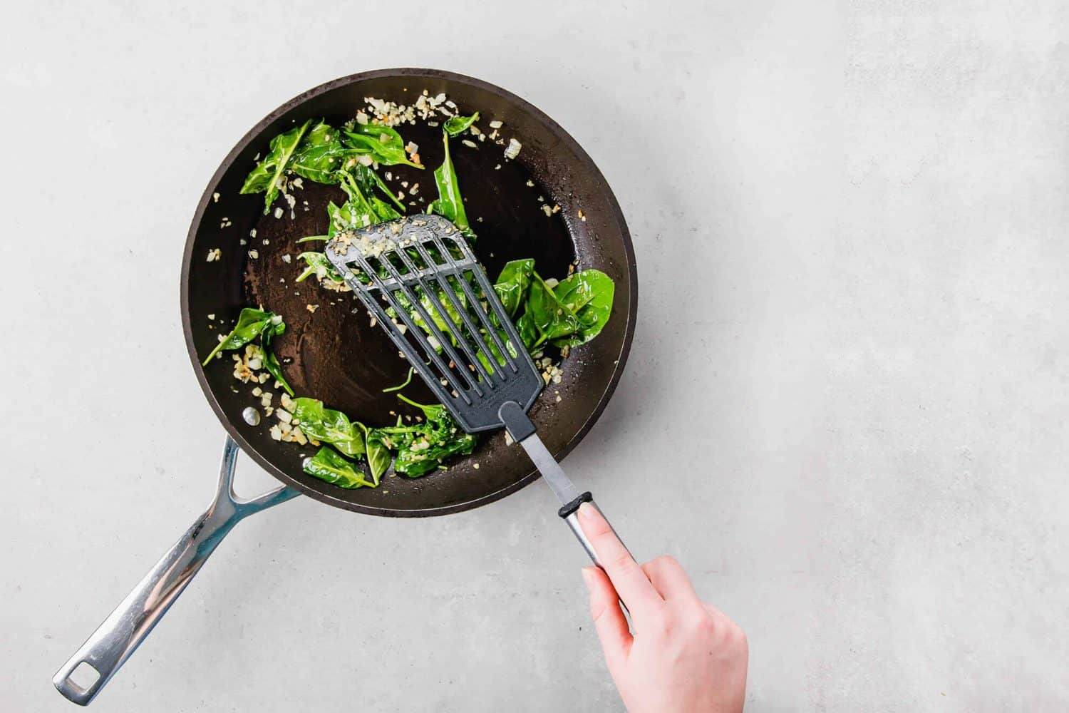 Overhead of skillet with Sauteed Kale and Onions, with hand holding spatula.