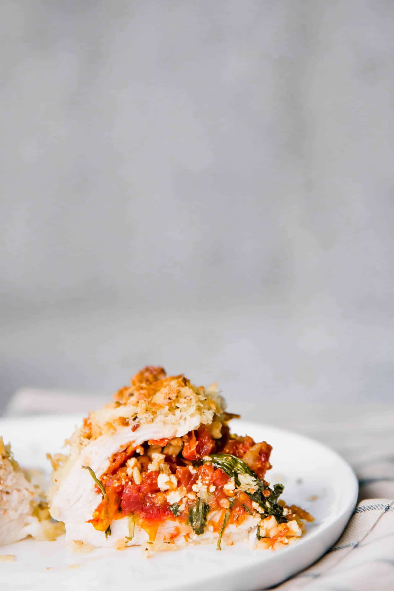 Partial image of stuffed chicken breast, cut in half, on white plate.