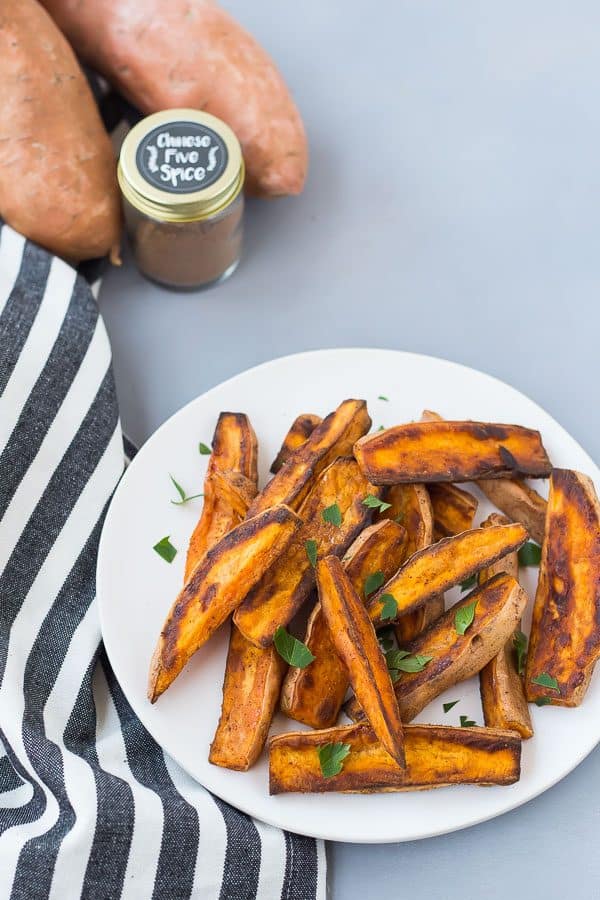 Plate of sweet potatoes, along with blue and white striped cloth, spice, and whole sweet potatoes.