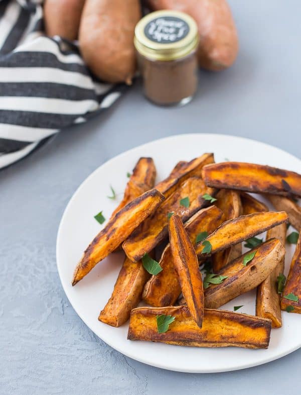 Plate of sweet potato wedges with jar of Chinese five spice and sweet potatoes in background.