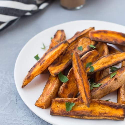 Sweet potato wedges on round white plate, garnished with chopped parsley.