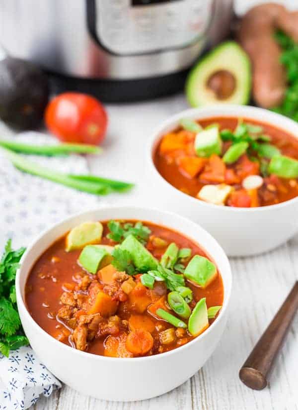 Two servings of chili in round white bowls, with spoon.