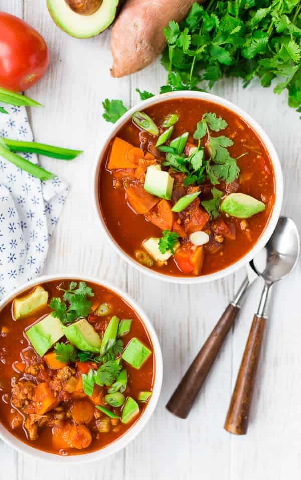 Overhead of two bowls of chili, garnished with cubed avocado, chopped green onion, and cilantro.