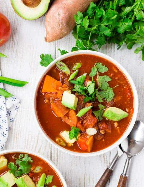 Overhead of chili in bowl with garnishes, on whitewashed board.