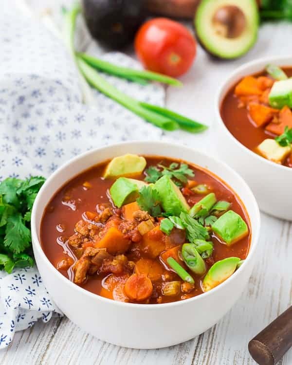 Closeup of a serving of chili in round white bowl, with garnishes.