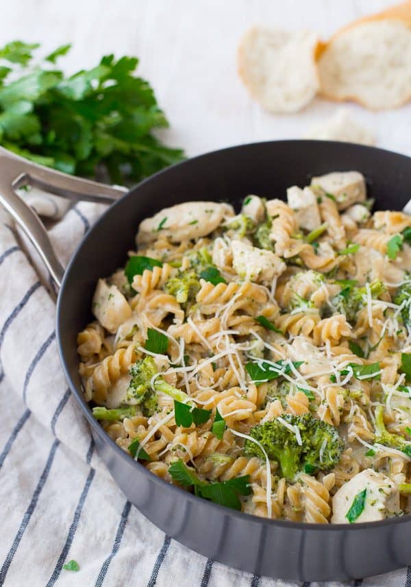Partial image of pasta in large pan with handle, bread and parsley in background.