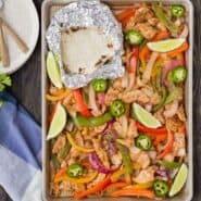Overhead of sheet pan with baked chicken fajitas, and foil wrapped tortillas.