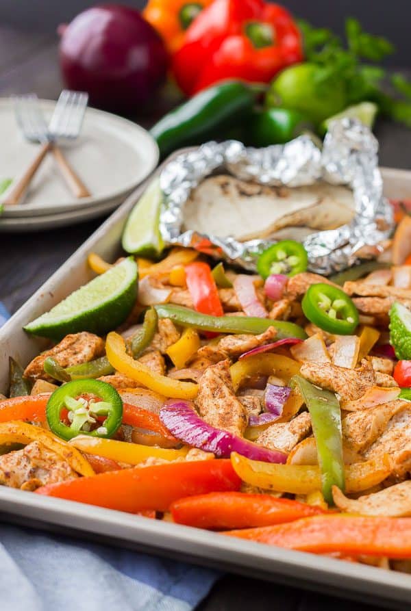 Partial image of sheet pan containing baked fajita ingredients, including foil wrapped tortillas.