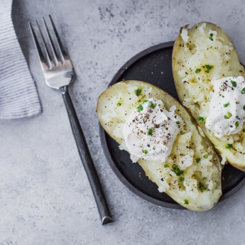 image of baked potato cut in half with sour cream and chives