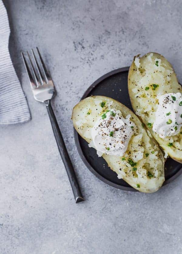 image of baked potato cut in half with sour cream and chives, on small black plate with fork alongside.