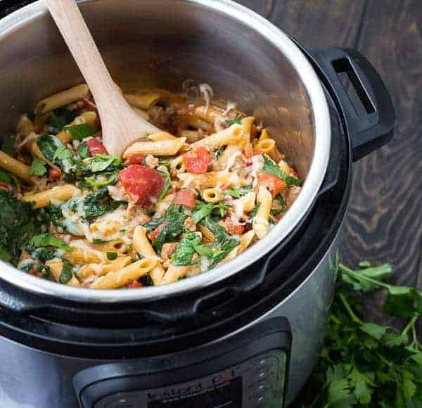 Pasta inside Instant Pot, garnished with chopped parsley, with wooden spoon.