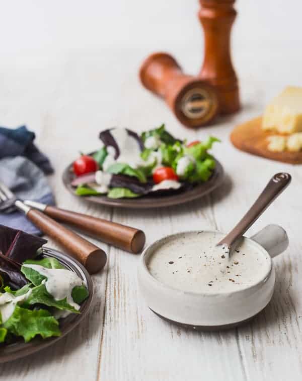 Parmesan Peppercorn Dressing in a small bowl, with a salad in the background.