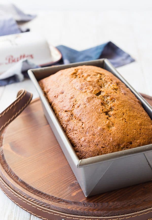 Banana bread in metal loaf pan on wooden tray.