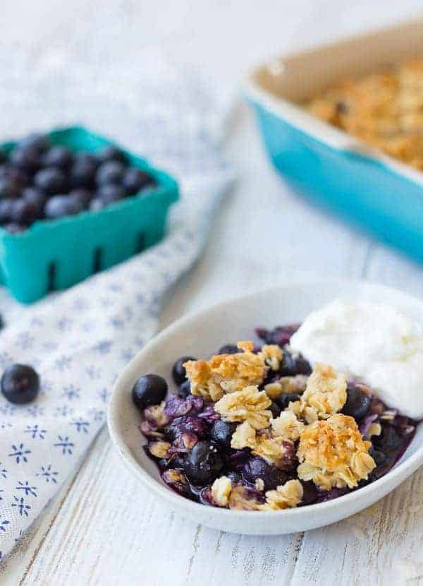 Small white oval dish containing a serving of blueberry crisp with yogurt.