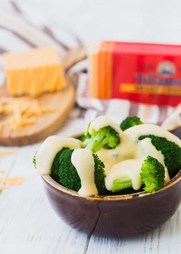 A round brown bowl containing steamed broccoli and cheese sauce.