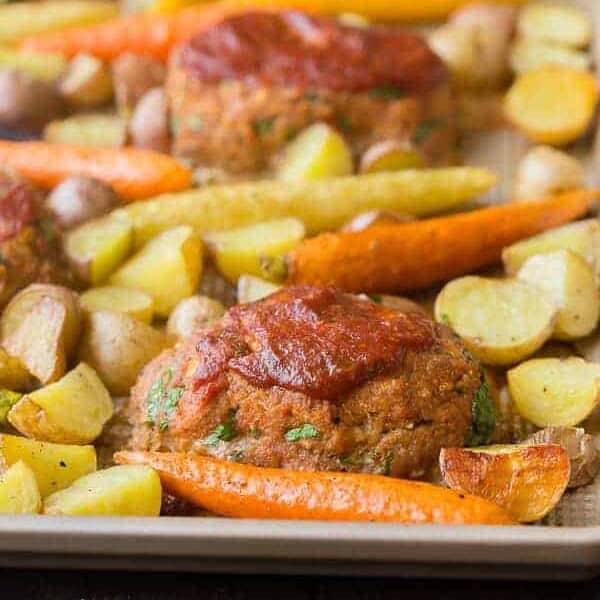 Mini meatloaves and roasted vegetables on sheet pan.