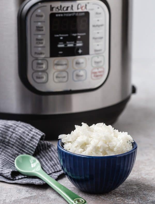 Small dark blue ceramic bowl containing a serving of rice, with Instant Pot in background.