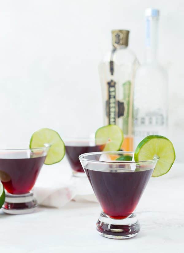 Front view of cherry martinis, with vodka and elderflower liqueur bottles in background.