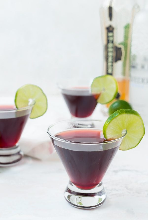 Front view of short martini glasses containing cherry martini, garnished with lime slice.