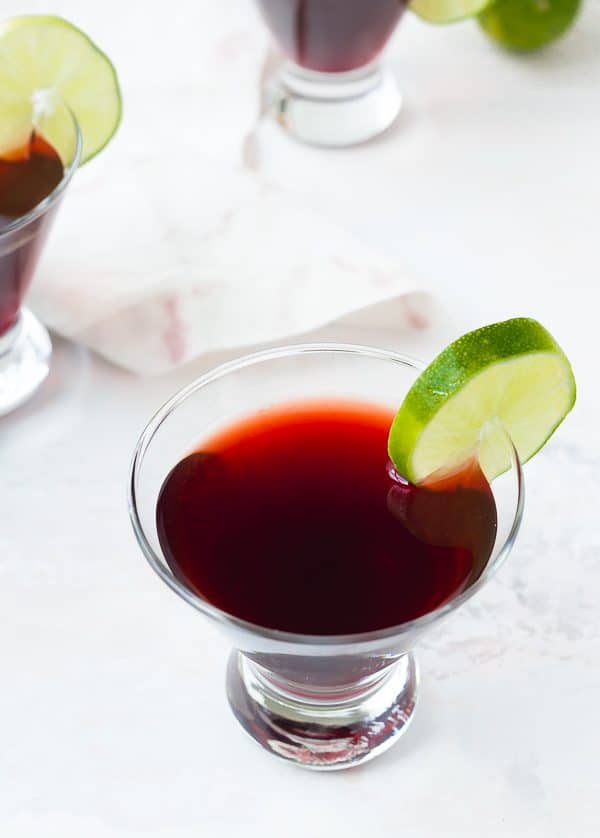 Overhead of cherry martini with lime slice garnish, on white background.