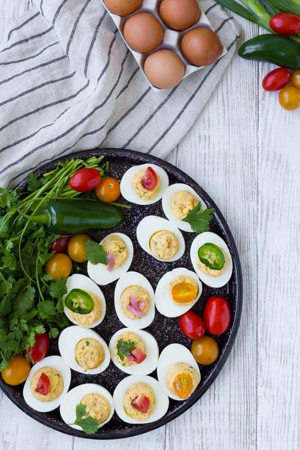 Overhead of black tray containing deviled eggs, tomatoes, jalapeno, and a bunch of cilantro.