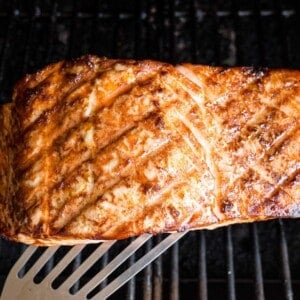 A spatula is used to lift a grilled salmon fillet from a grill.