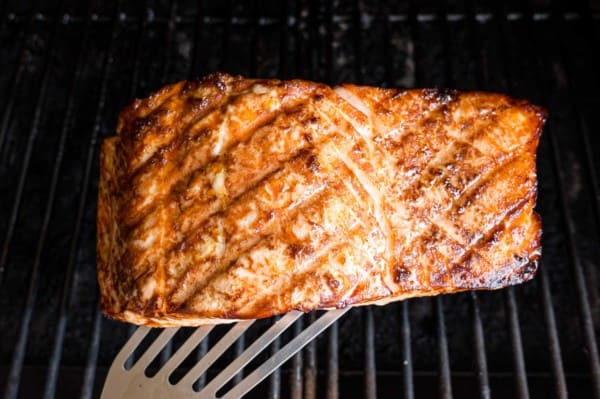 A spatula is used to lift a grilled salmon fillet from a grill.