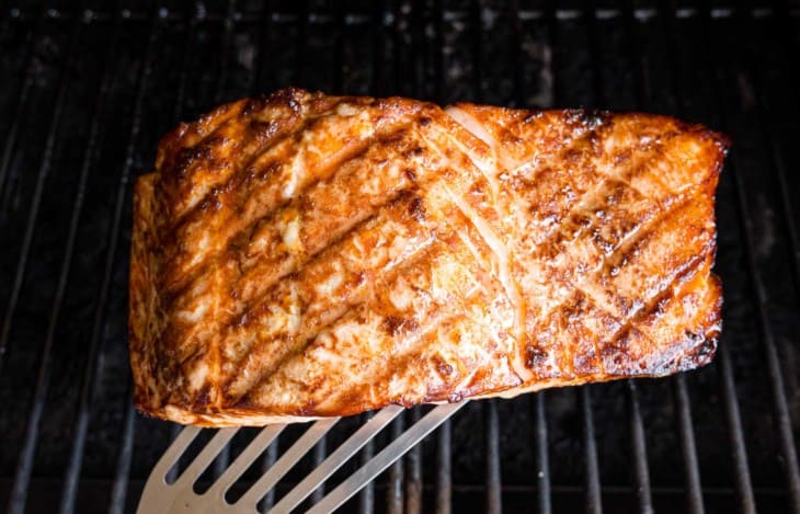 A spatula is used to lift a grilled salmon fillet from a grill.