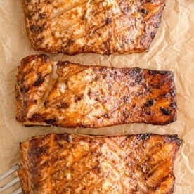 Overhead view of three grilled salmon fillets on parchment paper.