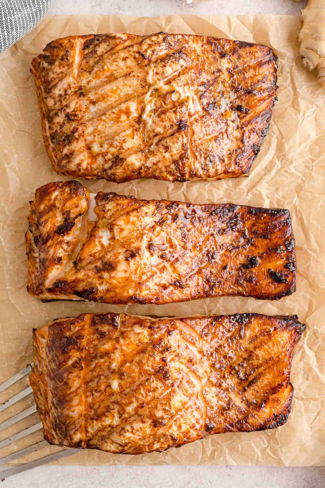 Overhead view of three grilled salmon fillets on parchment paper.