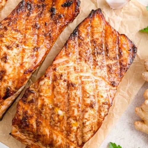 Overhead view of two grilled salmon fillets on parchment paper.