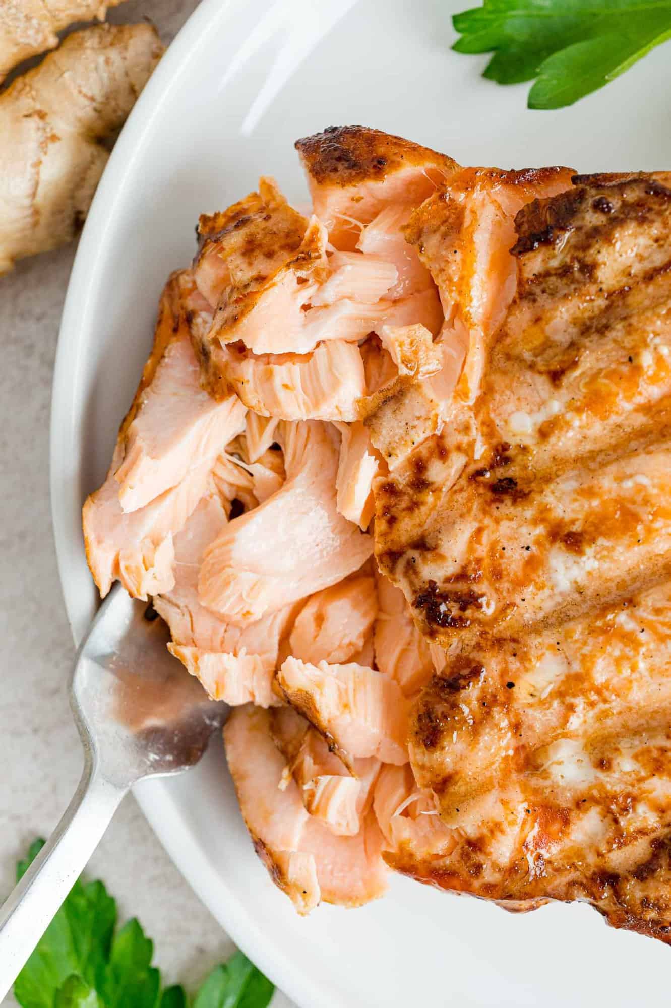 A fork stuck into flakes of grilled salmon on a white plate.