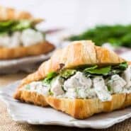 Chicken mixed with yogurt and dill on a split open croissant with greens.