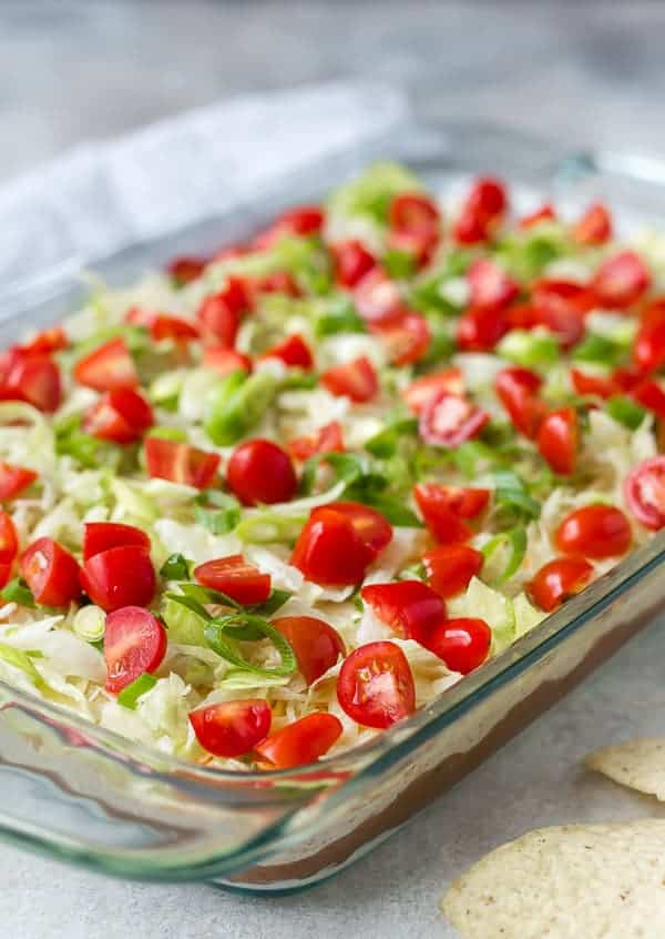 9x13 clear glass pan filled with layers of beans, cream cheese, lettuce and tomatoes.