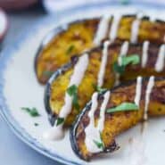 Three slices of roasted acorn squash on a blue rimmed white plate.