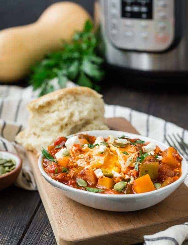 Small white oval bowl with fall-inspired shakshuka with squash, tomato sauce, and eggs. Bread is also pictured.