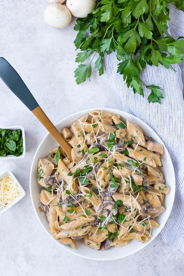 Overhead view of a white bowl filled with penne pasta, mushrooms, chicken, parsley, and parmesan.