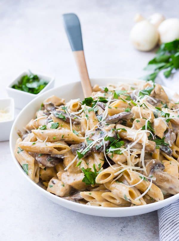 White bowl full of pasta with a creamy sauce, mushrooms, and chicken.