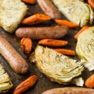 Sausage, cabbage slices, and carrots on a sheet pan, sprinkled with dill.