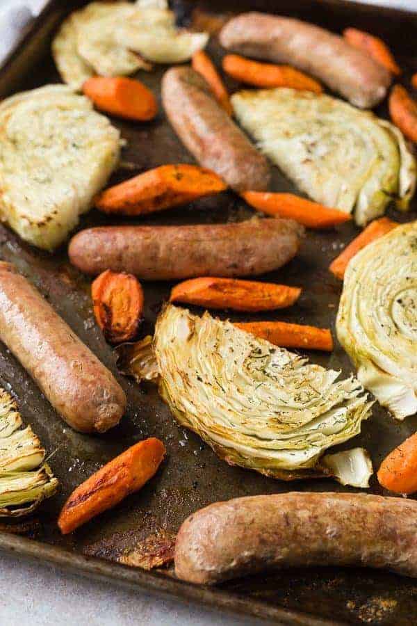 Sausage, cabbage slices, and carrots on a sheet pan, sprinkled with dill.