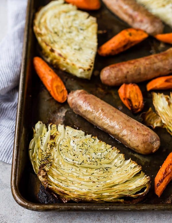 Close up view of a cabbage slice on a sheet pan, surrounded by sausage and carrots.