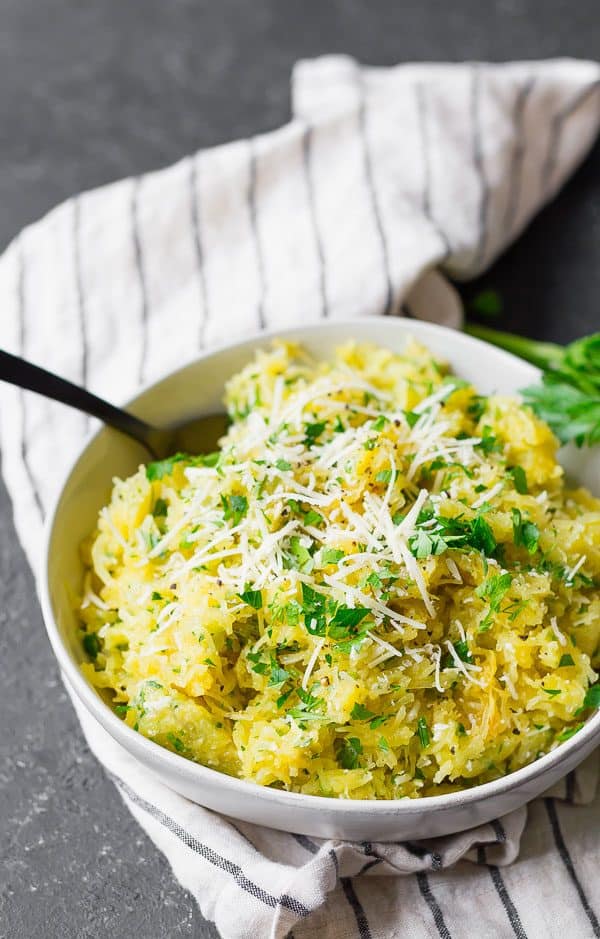 Spaghetti squash in a white bowl with a black spoon, topped with herbs and cheese.