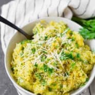 Spaghetti squash in a white bowl sprinkled with green parsley and white parmesan cheese.