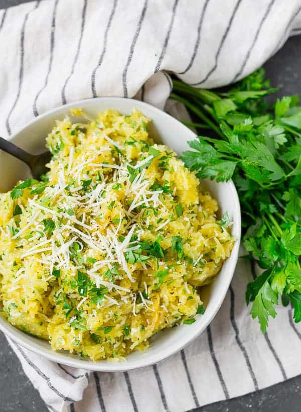 Overhead view of yellow spaghetti squash in a bowl with a black spoon. Fresh parsley is also pictured.