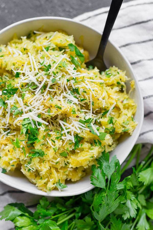 Overhead view of a bowl of spaghetti squash sprinkled with herbs and grated parmesan.